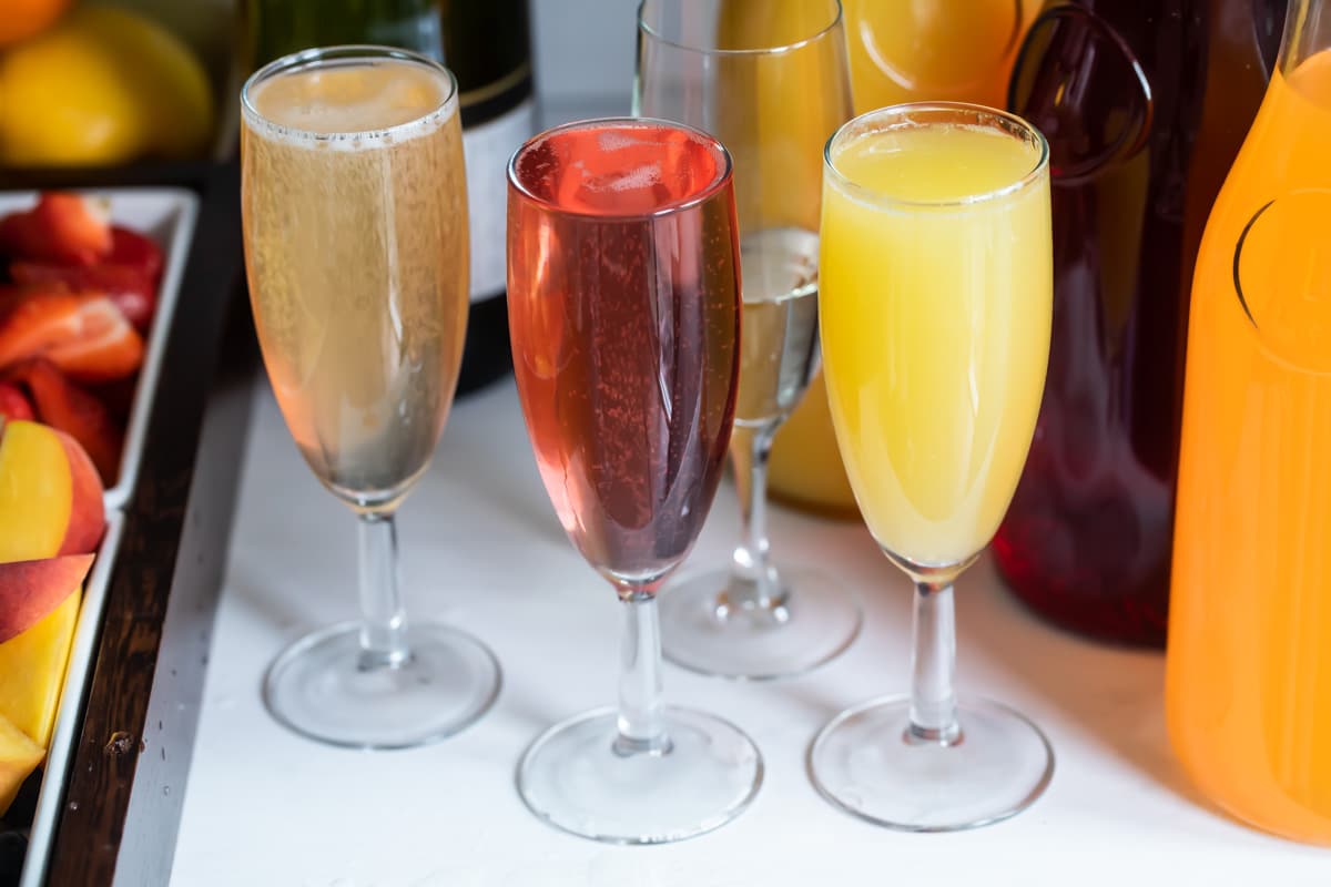 Carafes of juice, bottles of sparkling wine, and fresh fruit garnishes for a mimosa bar.