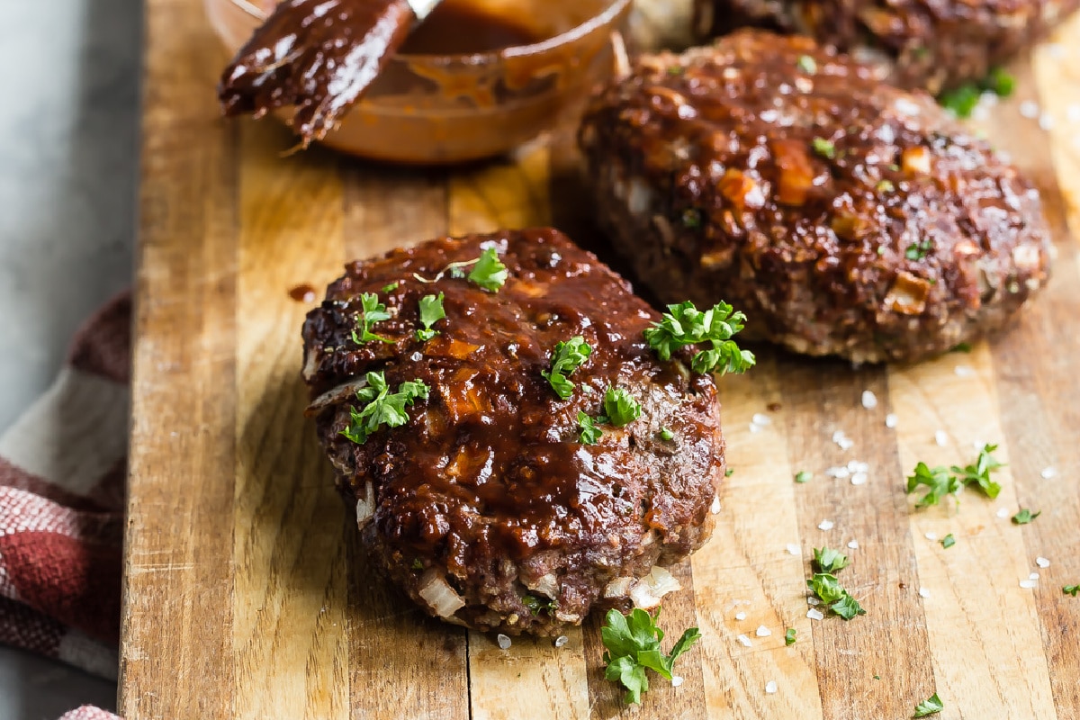 Mini meatloaves with balsamic glaze on a wooden cutting board.