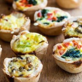 A wooden board filled with 4 varieties of mini quiche.