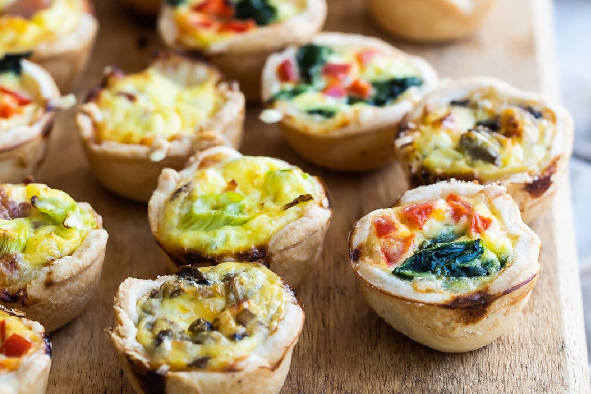 A wooden board filled with 4 varieties of mini quiche.