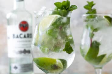 Two mojito cocktails in glasses with a bottle of white rum in the background.