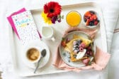 A Mother's Day breakfast tray with crepes, orange juice, coffee, fresh flowers, and a greeting card.