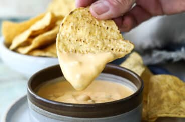 A tortilla chip being dipped in nacho cheese.