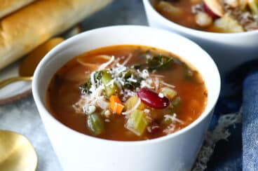Two bowls of Olive Garden Minestrone soup next to breadsticks.
