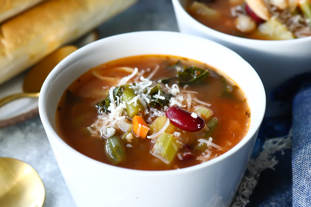 Two bowls of Olive Garden Minestrone soup next to breadsticks.