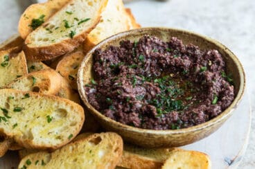 Homemade olive tapenade in a bowl surrounded by toasted bread.
