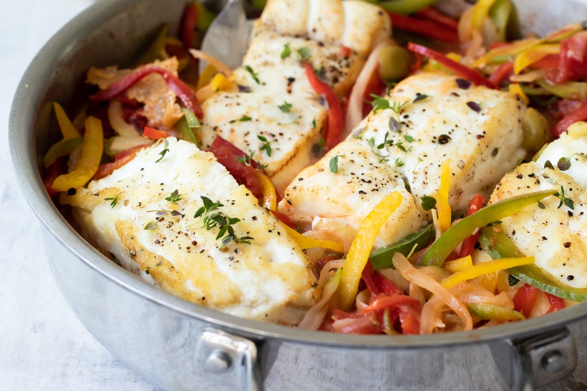Pan-Seared Halibut with peppers and olives in a silver skillet.