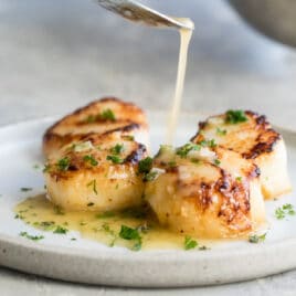 Lemon butter sauce being drizzled onto pan-seared scallops.