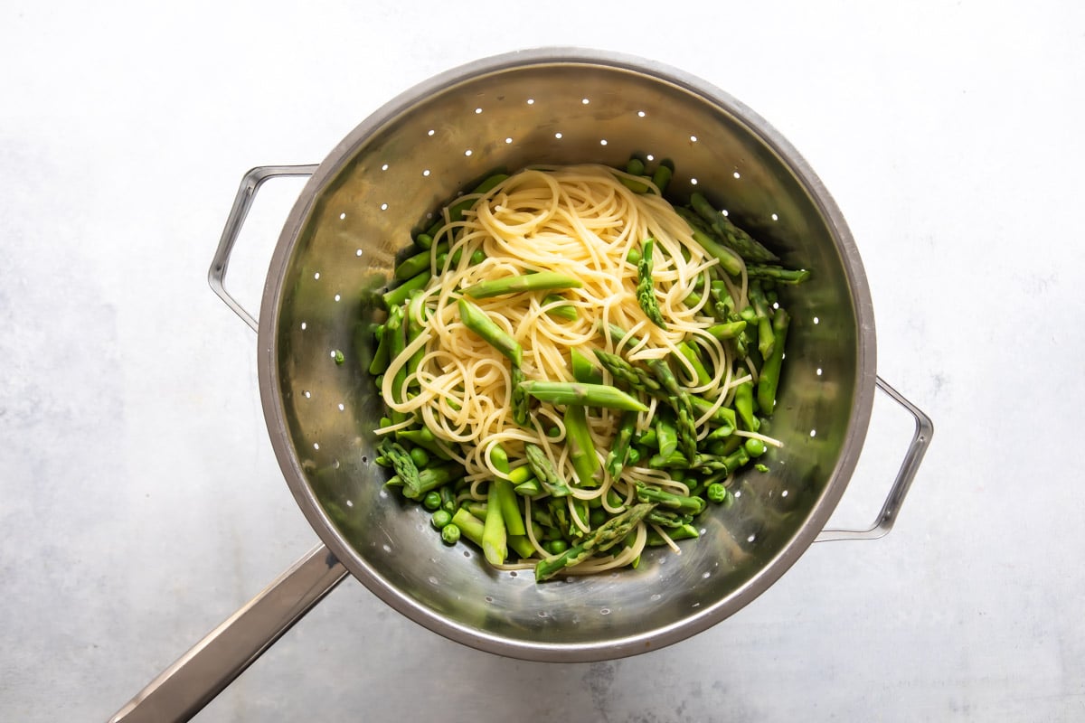 Pasta, peas, and asparagus in a silver colander.