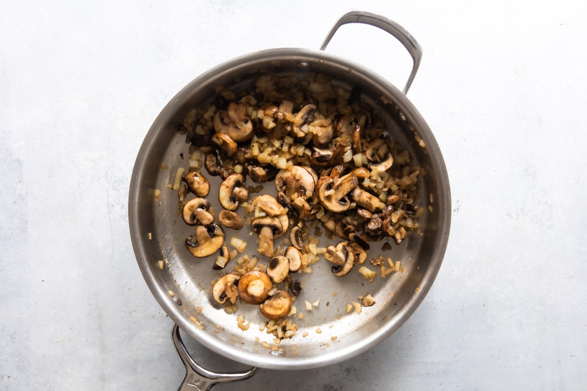 A skillet with cooked mushrooms and onions in it.