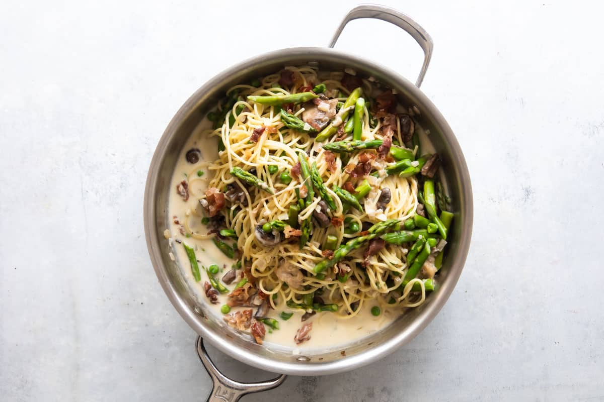 Pasta with peas and prosciutto in a silver skillet.