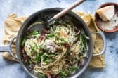 Pasta with peas and prosciutto in a silver skillet.
