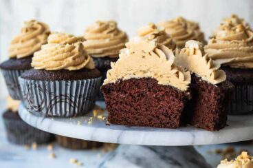 A cake stand filled with chocolate cupcakes with peanut butter frosting, 1 cut open to show the inside.