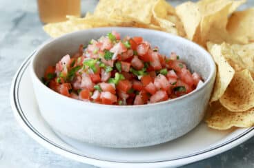 A bowl of pico de gallo on a plate with tortilla chips.