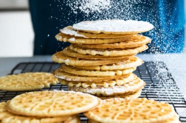 Pizzelle cookies being dusted with powdered sugar.