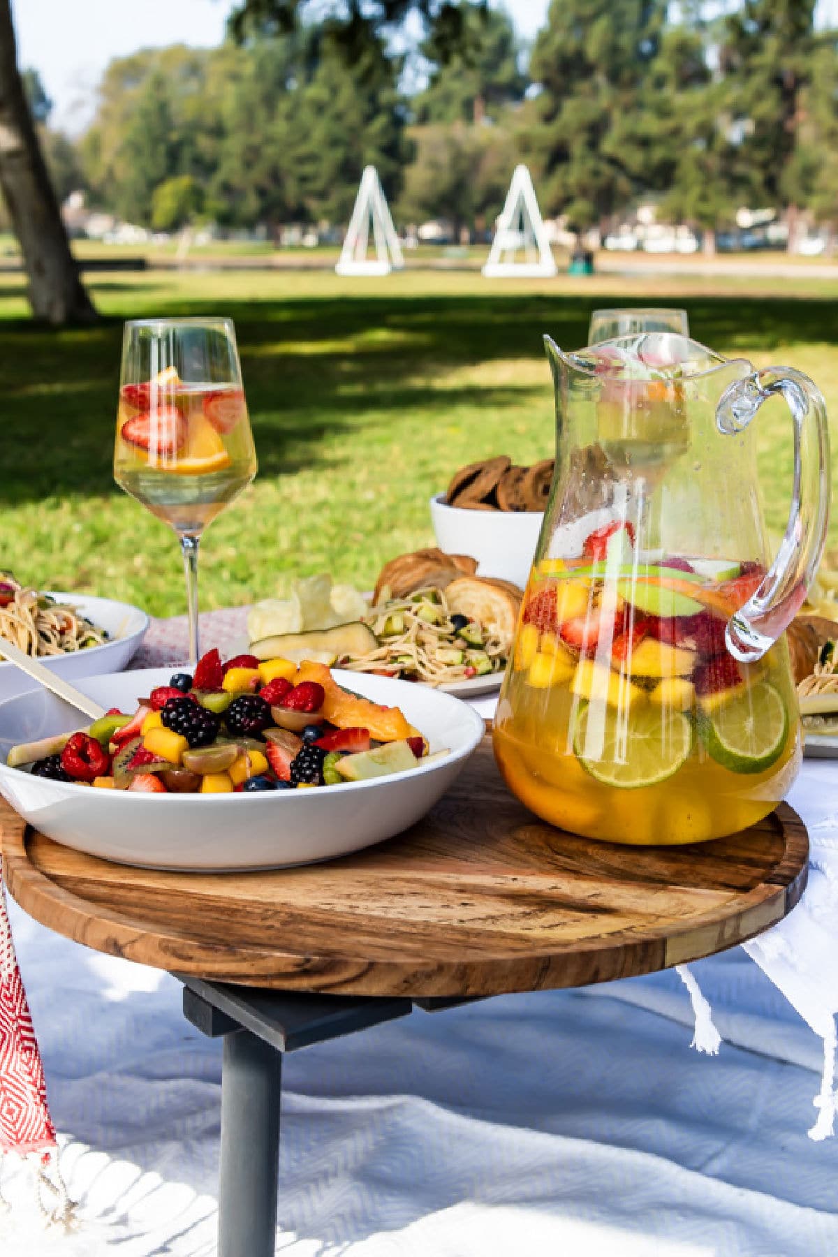 A setup for a picnic in a park with sangria and fruit salad.