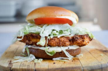 A pork tenderloin sandwich on a wooden cutting board.