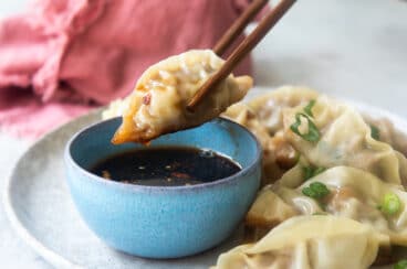 A platter of potstickers, someone holding one with chopsticks.