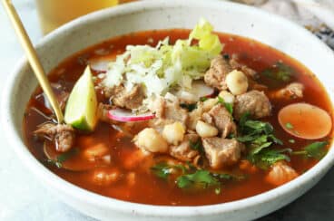 A bowl of pozole rojo next to a bottle of Modelo.