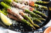 Prosciutto wrapped asparagus on a black plate with shredded Parmesan.
