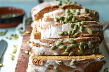 A loaf of pumpkin bread sliced on a wooden cutting board.