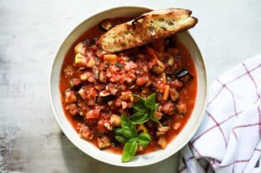 A bowl full of ratatouille stew with grilled bread on the side.