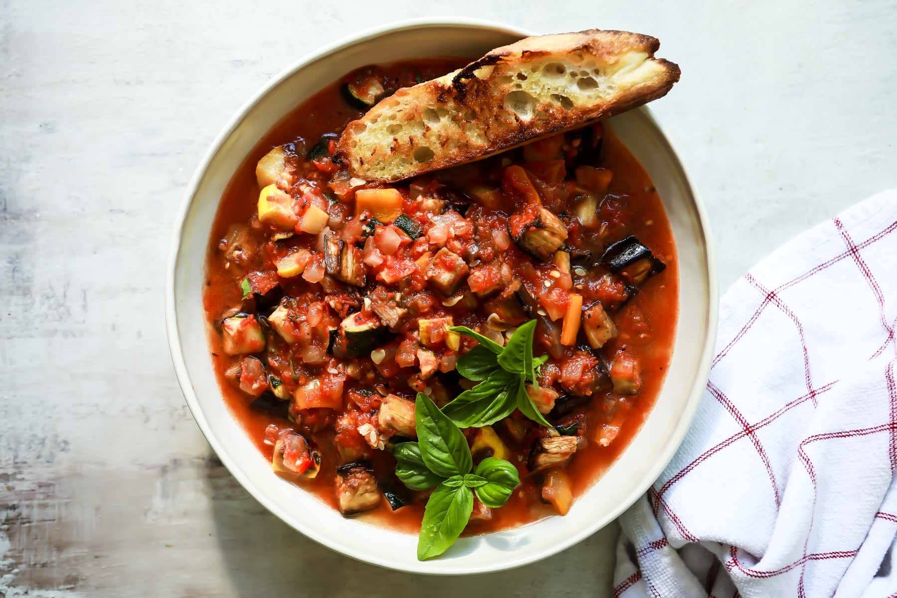 A bowl full of ratatouille stew with grilled bread on the side.