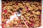 A pan of rhubarb crisp with a spoon resting in it.