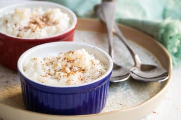 Rice pudding in two ramekins on a plate next to two spoons.