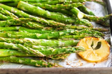 A baking sheet full of roasted asparagus with lemons.