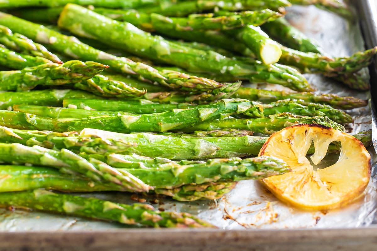 A baking sheet full of roasted asparagus with lemons.