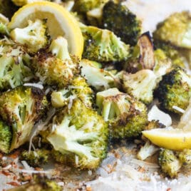 Roasted broccoli on a baking sheet with lemon garnish.