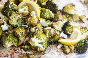 Roasted broccoli on a baking sheet with lemon garnish.