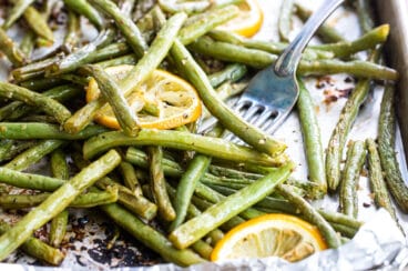Roasted green beans on a baking sheet with lemon garnish.