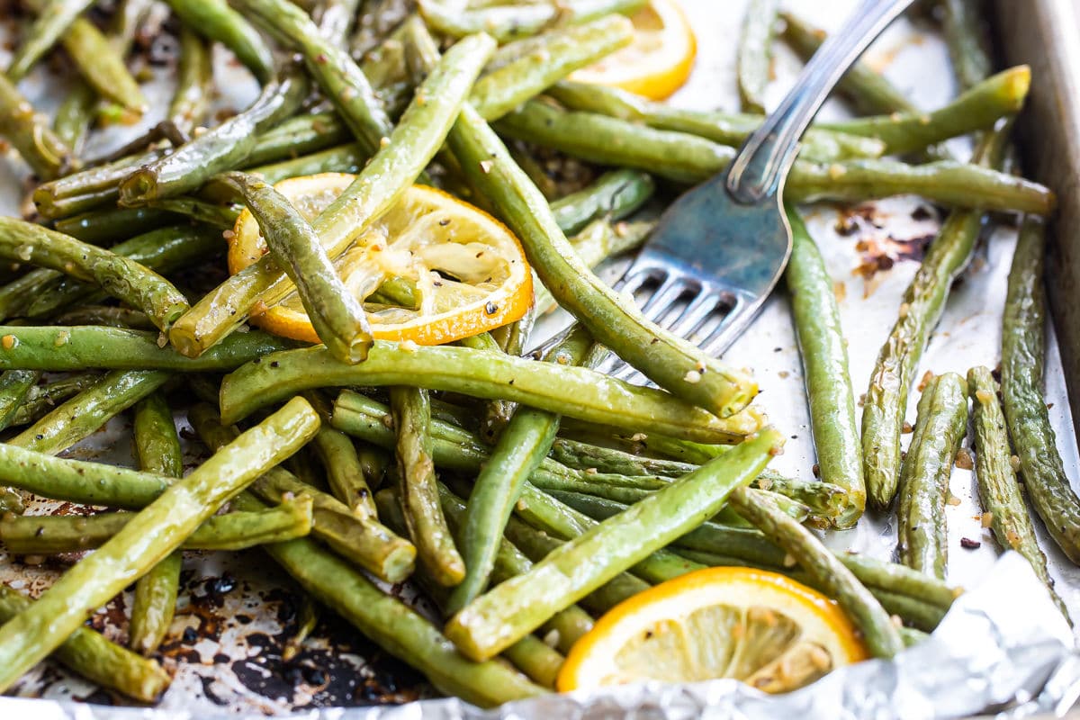 Roasted green beans on a baking sheet with lemon garnish.
