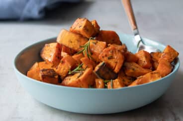 A bowl of roasted sweet potoates with a spoon resting in it.