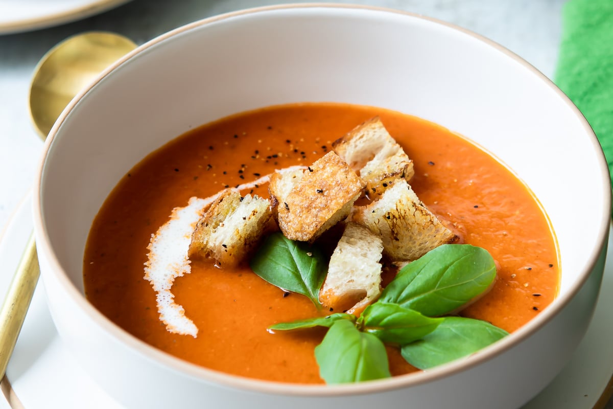 A bowl of roasted tomato soup garnished with basil and croutons.