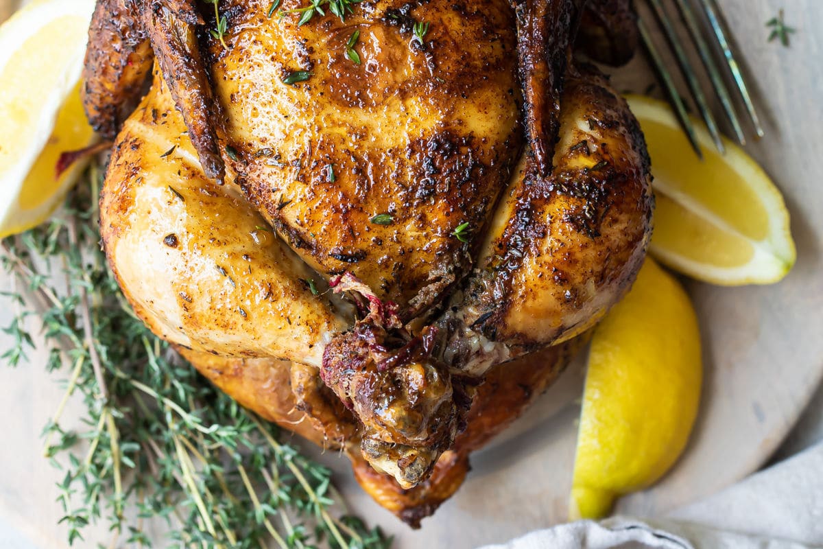 A rotisserie chicken on a white plate with slices of lemon.