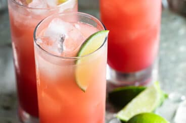 Seabreeze cocktail in three glasses on a silver serving tray with ice and sliced and whole limes.