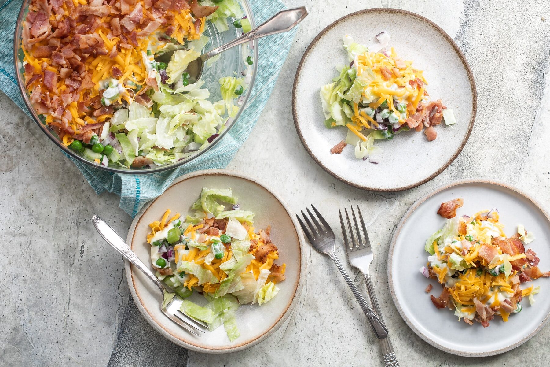 A bowl of seven layer salad surrounded by three smaller plates with servings of seven layer salad.