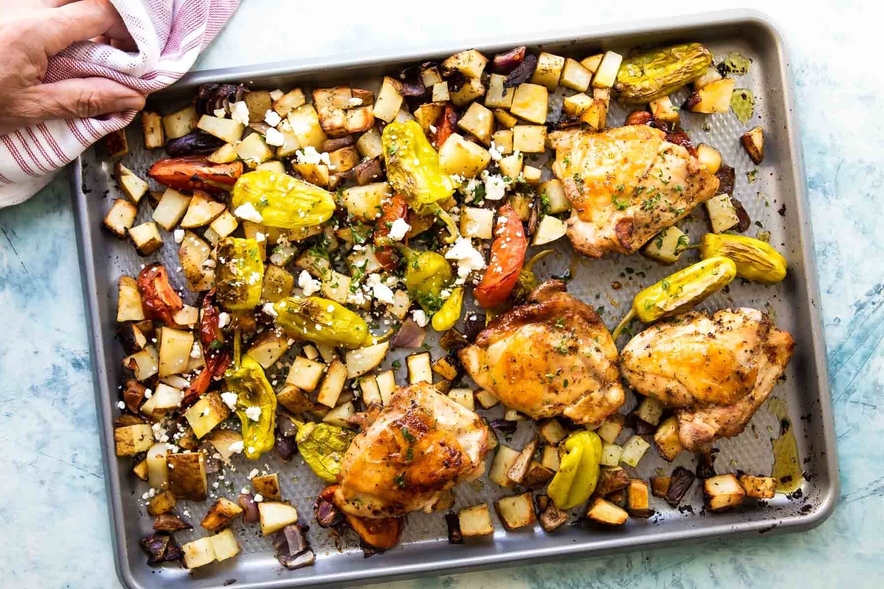 Sheet pan Greek chicken being set on a countertop.