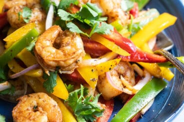 Shrimp fajitas on a blue plate with a side of rice and flour tortillas.