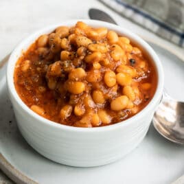 Slow cooker baked beans in a small white bowl.