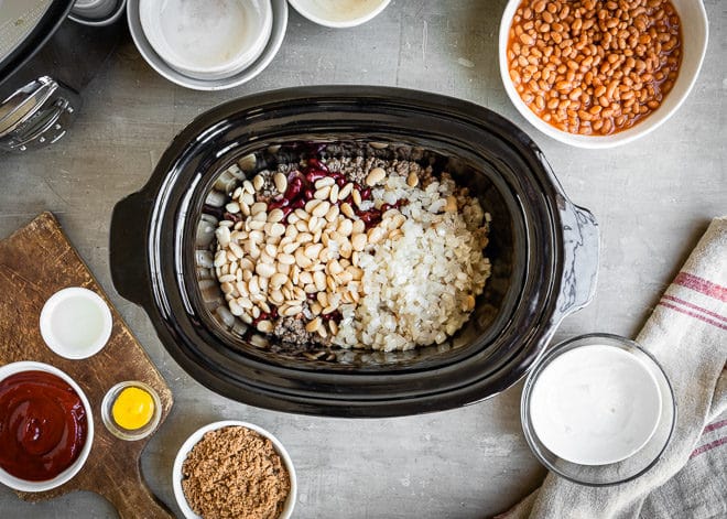 Slow cooker calico beans ingredients in a black slow cooker and in various bowls.
