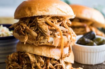 Two pulled chicken sandwiches stacked on top of each other on a baking sheet.
