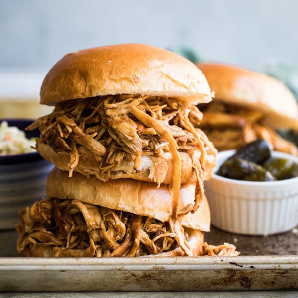 Two pulled chicken sandwiches stacked on top of each other on a baking sheet.