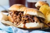 A plated with pulled pork sandwiches and chips on it.