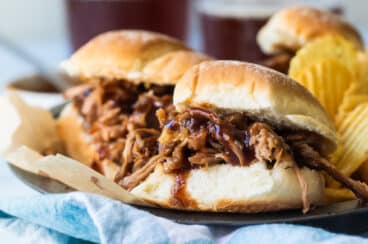 A plated with pulled pork sandwiches and chips on it.