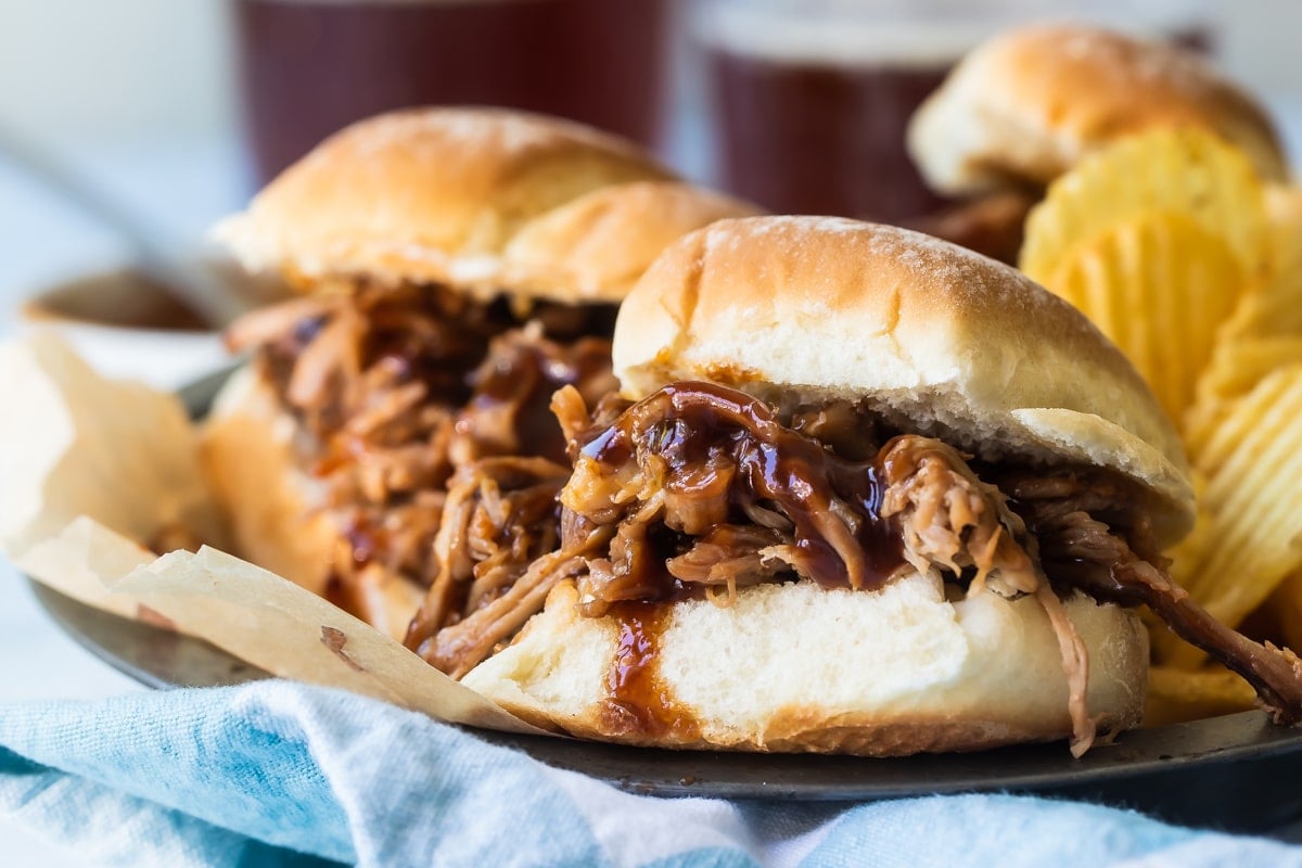 A plated with pulled pork sandwiches and chips on it.