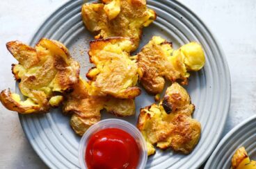Smashed potatoes on three small gray plates.